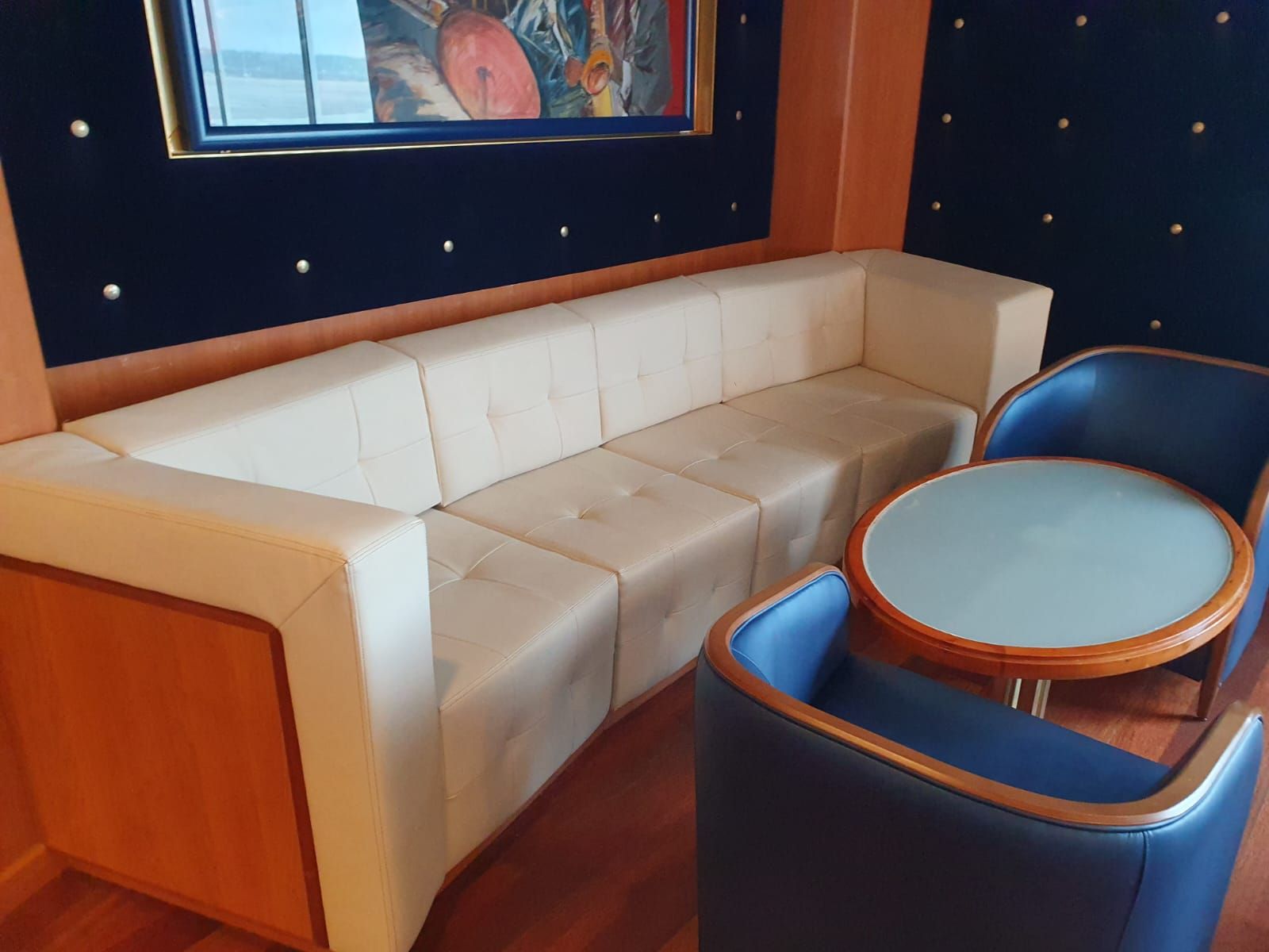 Canapé beige en L avec une table ronde et deux fauteuils bleus dans une pièce avec un mur bleu marine et des boiseries.