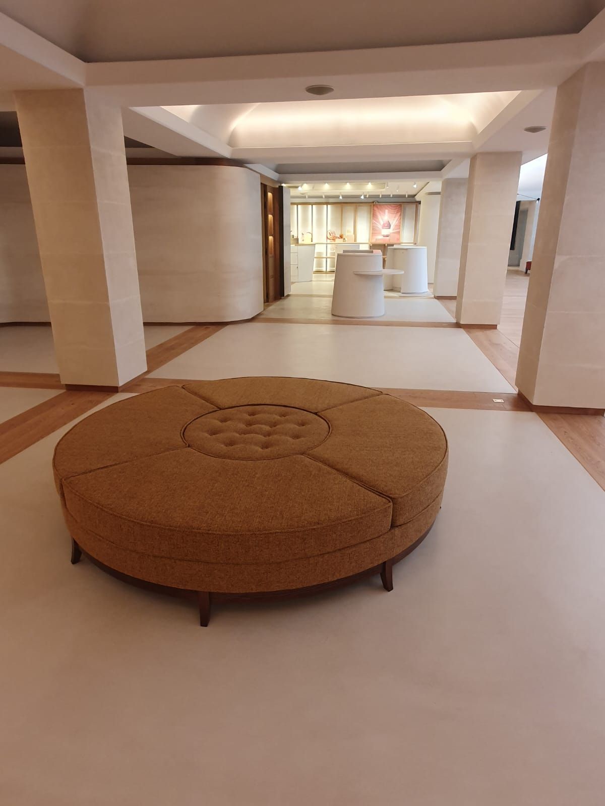 Un grand pouf rond dans un hall de couleur claire avec des colonnes, menant à un espace très éclairé avec des tables blanches.