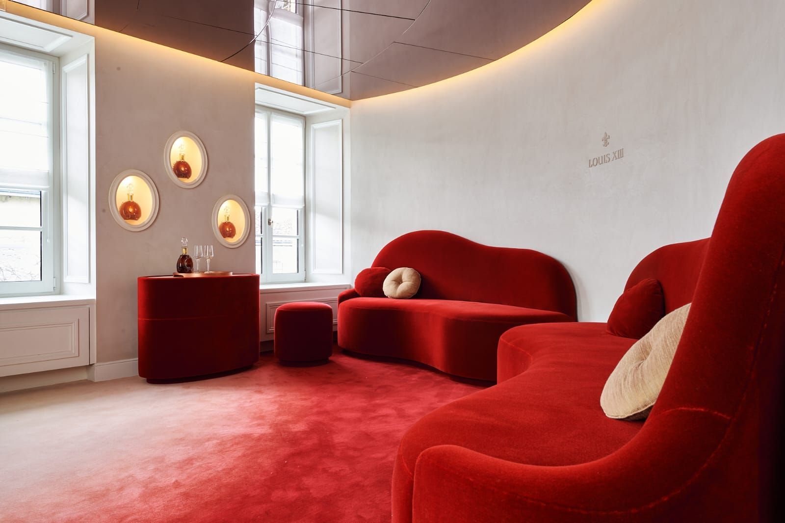 Un salon luxueux sur le thème rouge avec des canapés incurvés, un tapis rouge et des appliques murales en forme d'orbe.