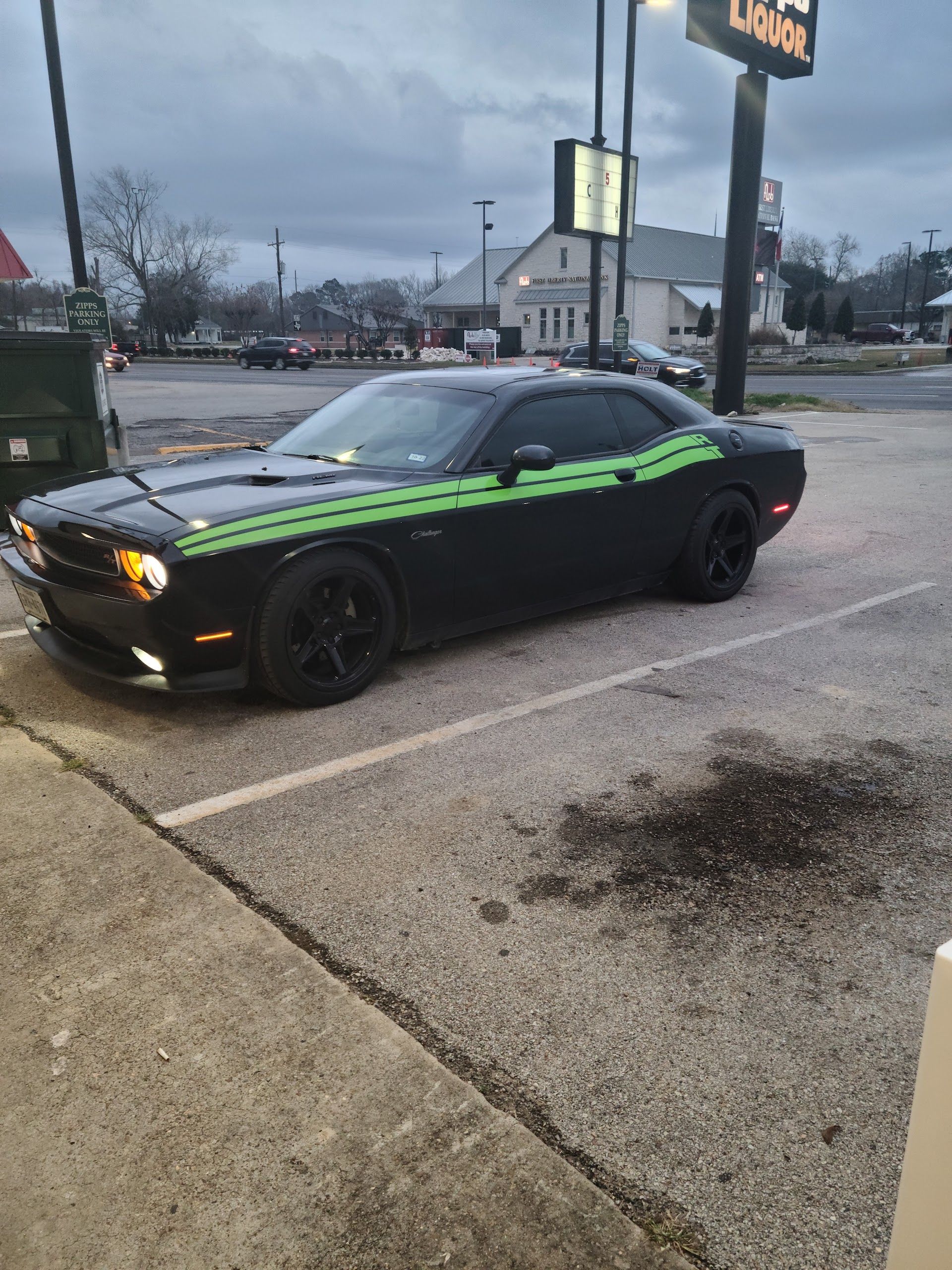 Black Dodge Challenger with green stripes parked in a lot near a Dunkin' Donuts sign.