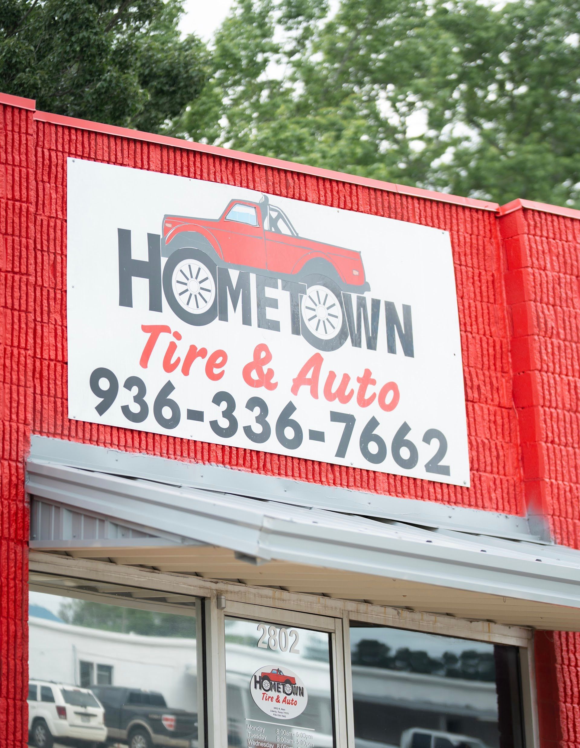 Sign for Hometown Tire & Auto with a red truck graphic and phone number 936-336-7662 on a red brick building.