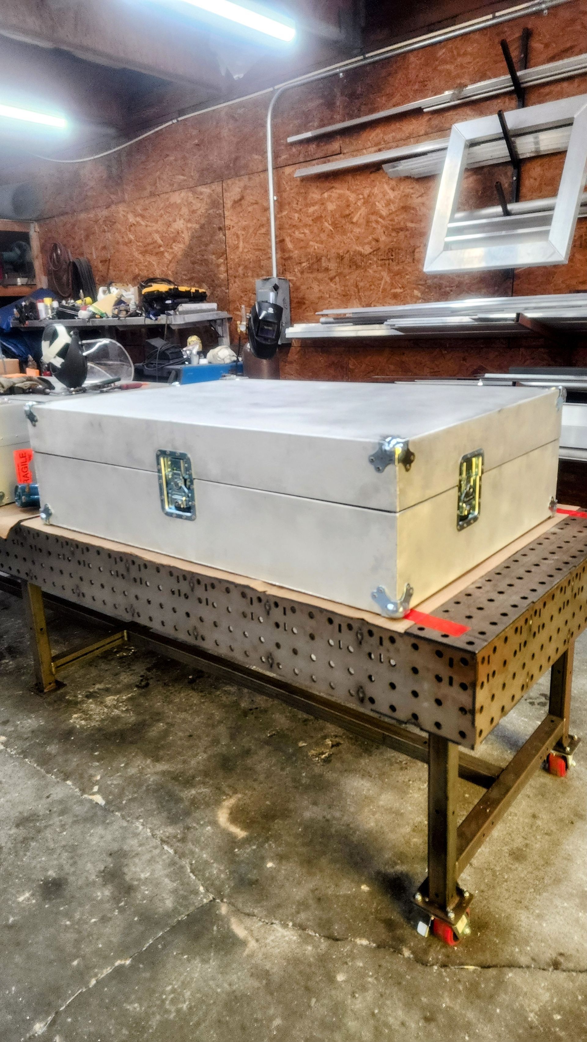 Large, silver box with clasps on a metal welding table in a workshop.