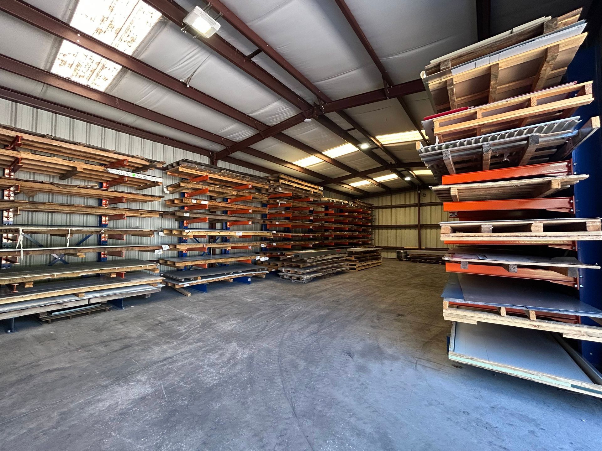 Warehouse interior with shelves of metal sheets and pallets.
