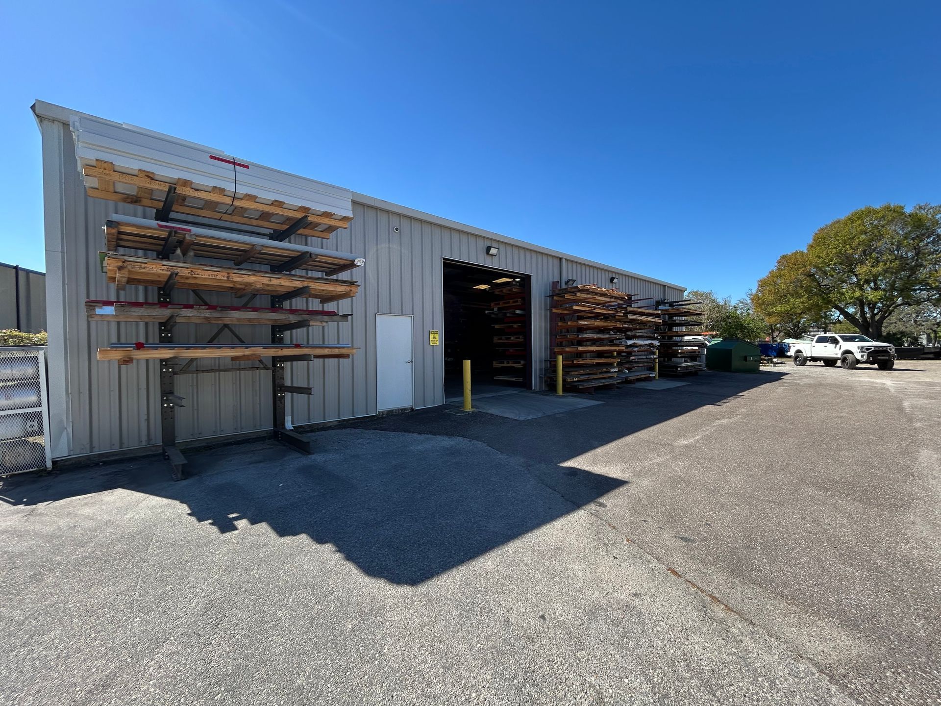 A gray metal warehouse with wood shelves outside and inside, under a blue sky.