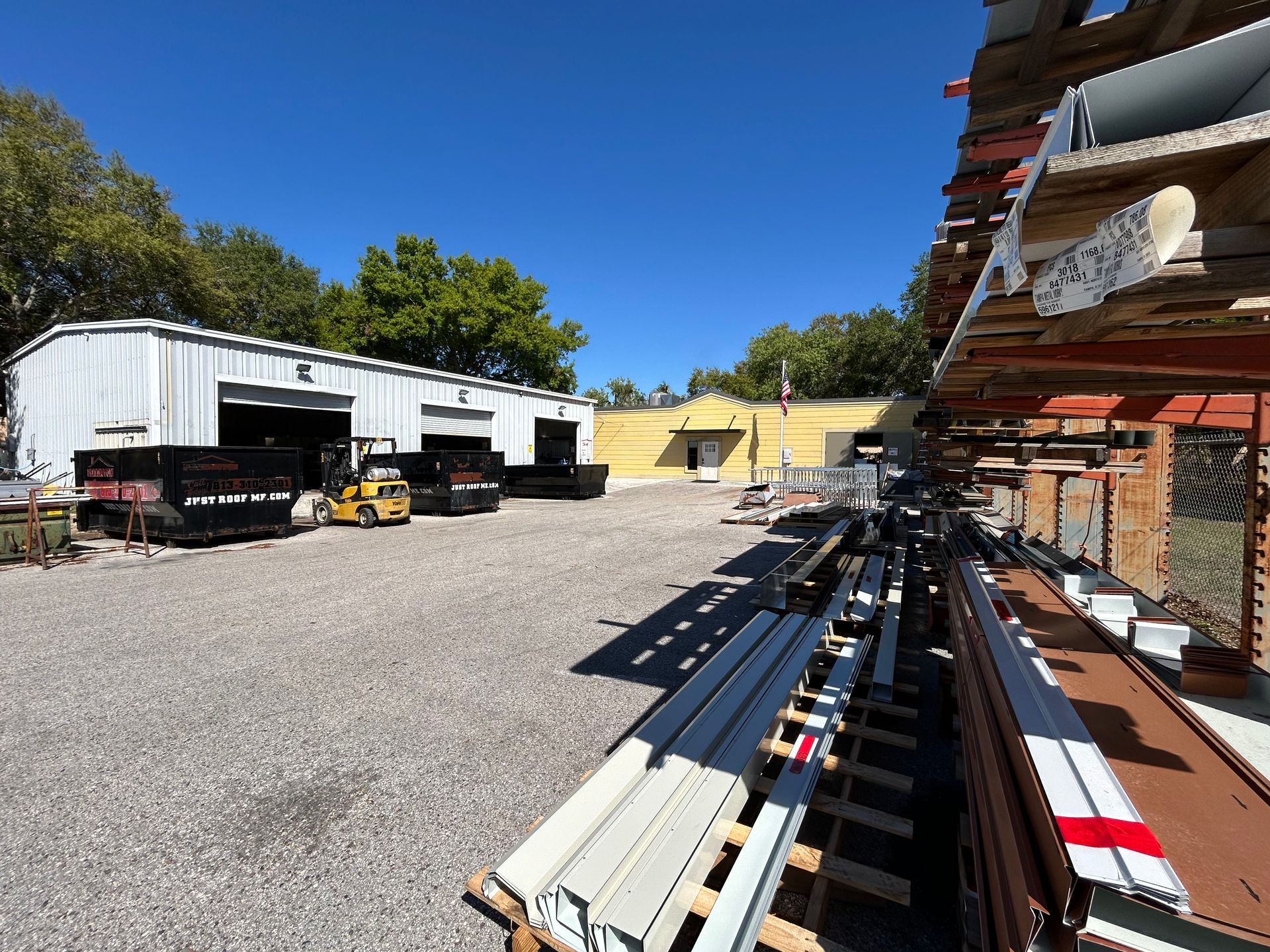 A building supply yard with materials, a forklift, and buildings under a bright blue sky.