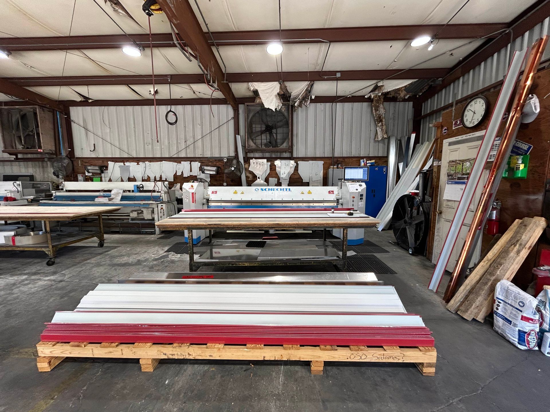 A metal fabrication shop with stacked metal panels in red, white, and silver; machinery, and worktables.