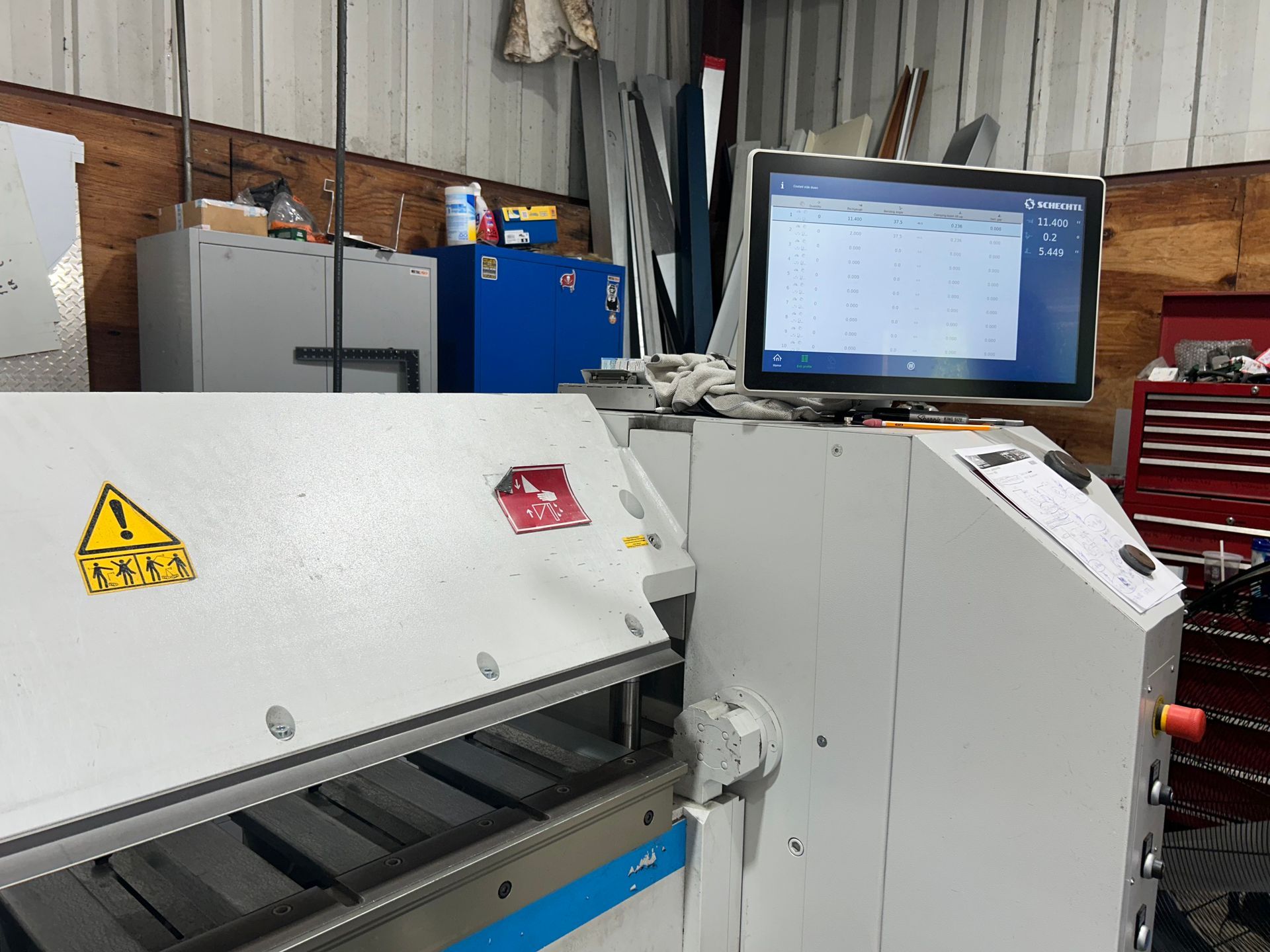 A white industrial machine with a computer screen displaying data, inside a workshop.