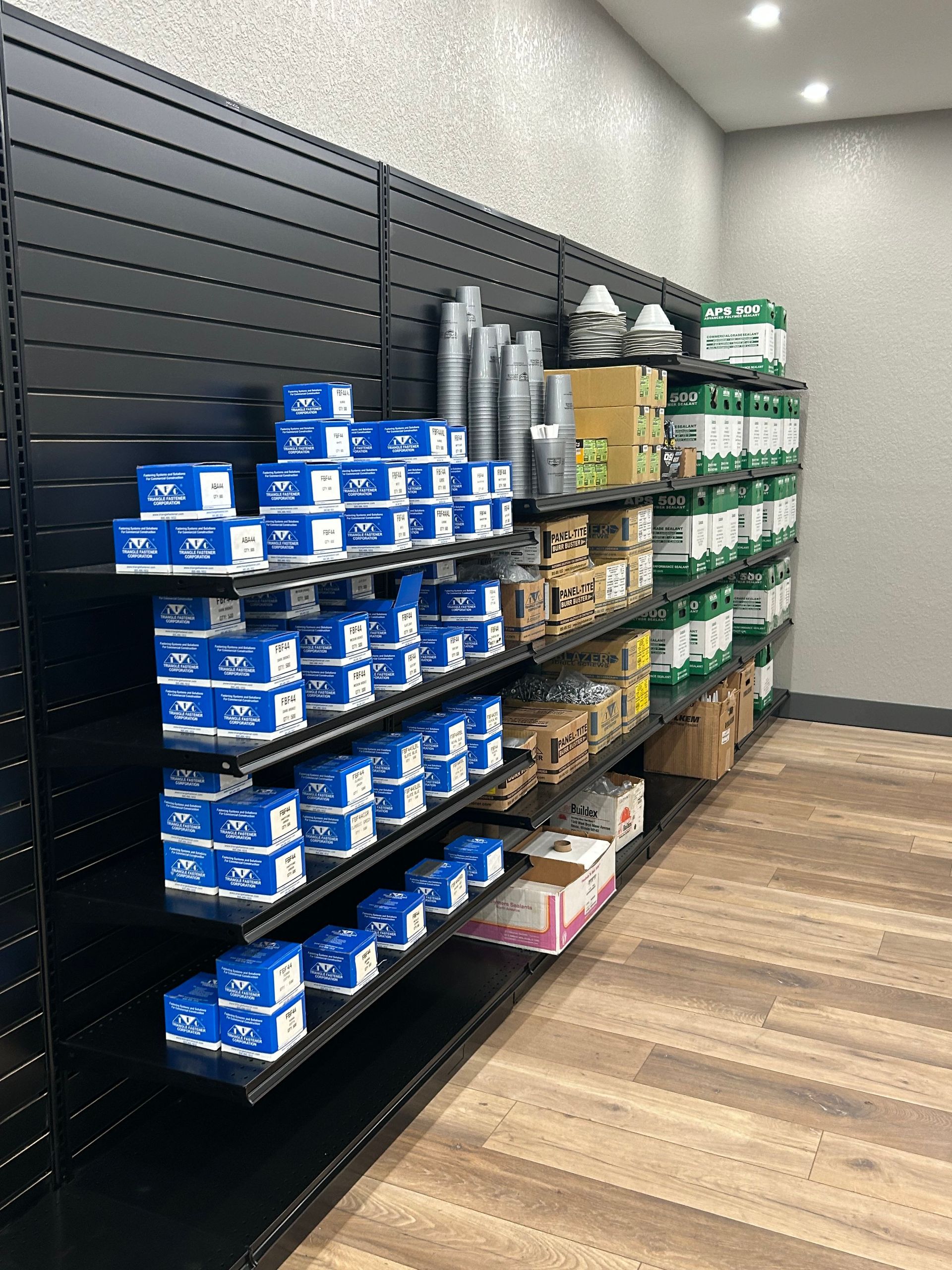 Shelves stocked with blue boxes, cylindrical cans, and other items in a store with black walls and wood flooring.