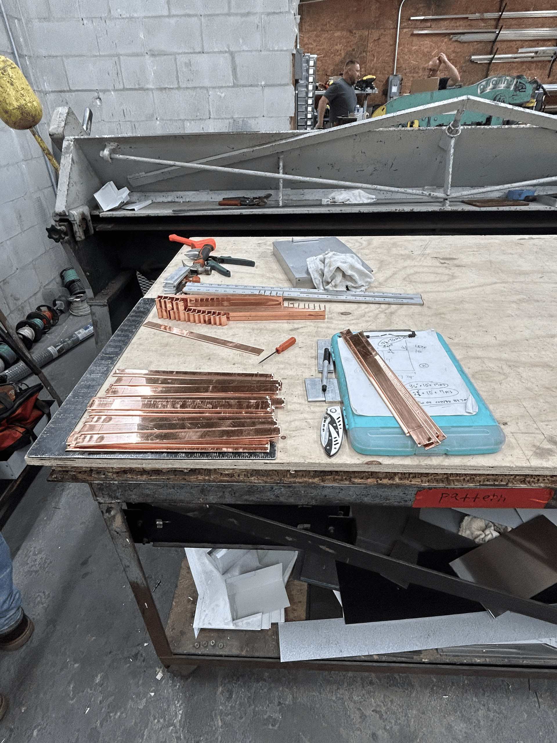 Workbench with copper strips, tools, and a clipboard in a workshop.