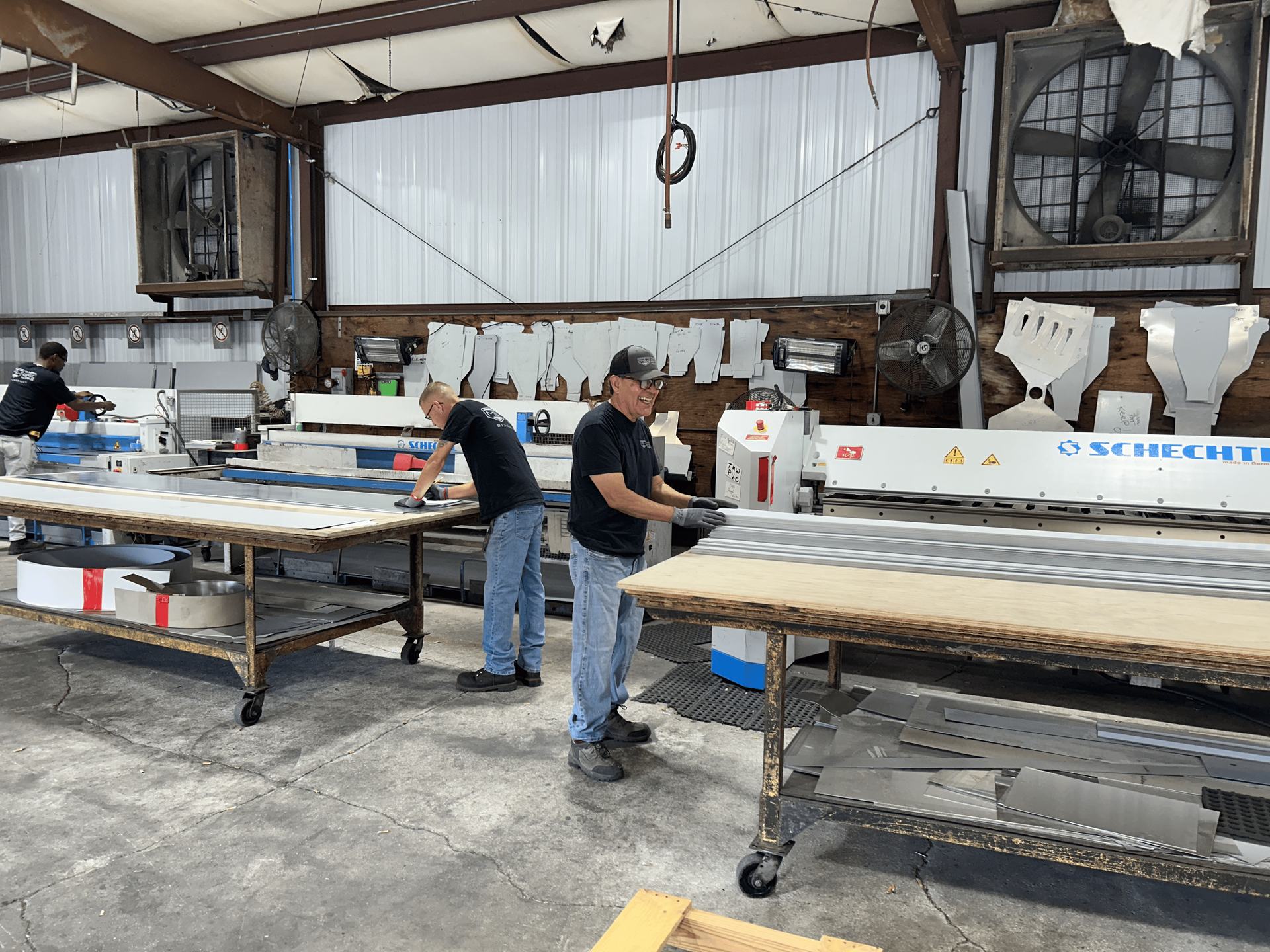 Men working in a manufacturing facility, operating machinery. Tables with materials are in the foreground.