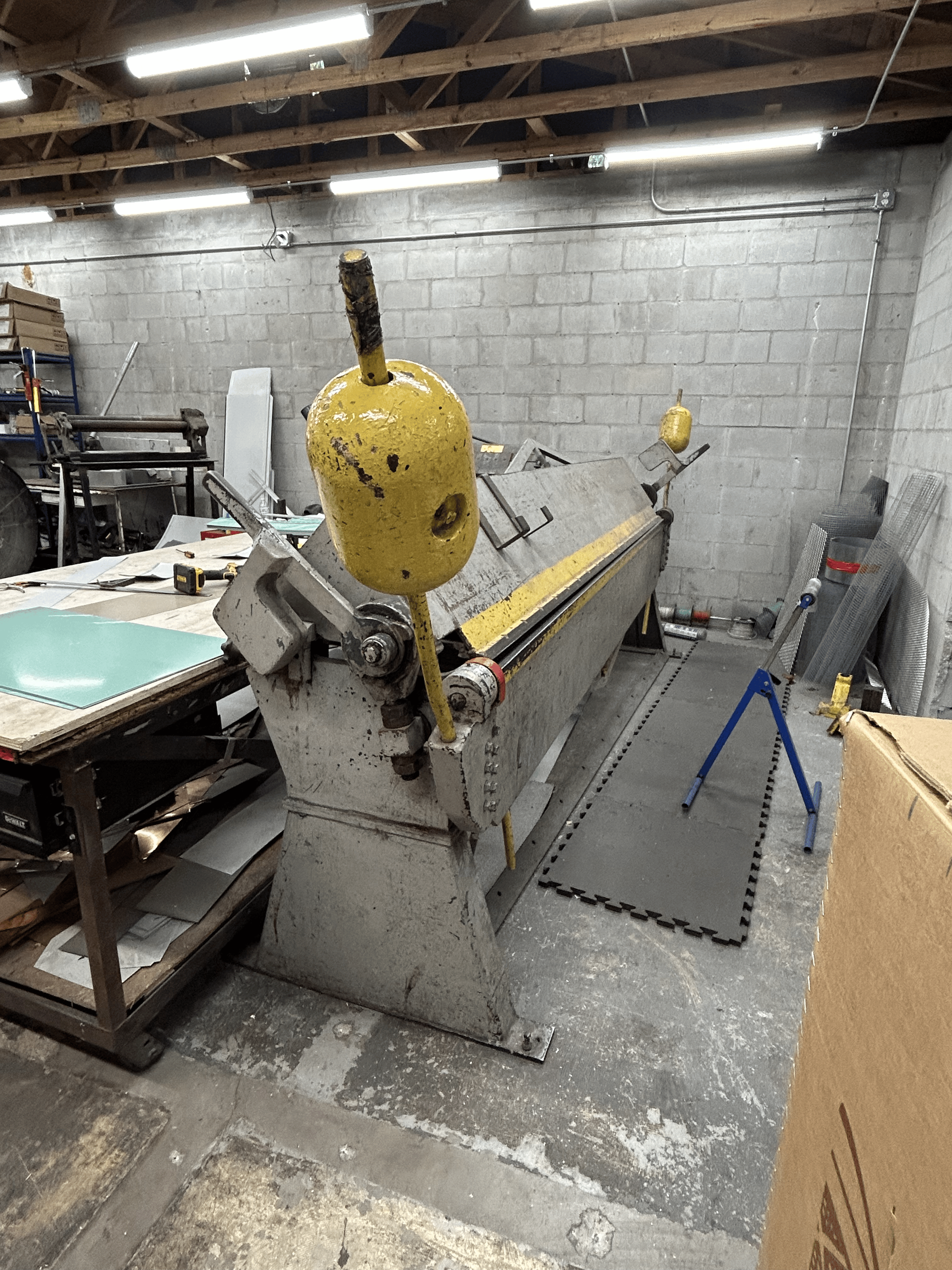 Metal bending machine in a workshop. Yellow handle and support, gray body.