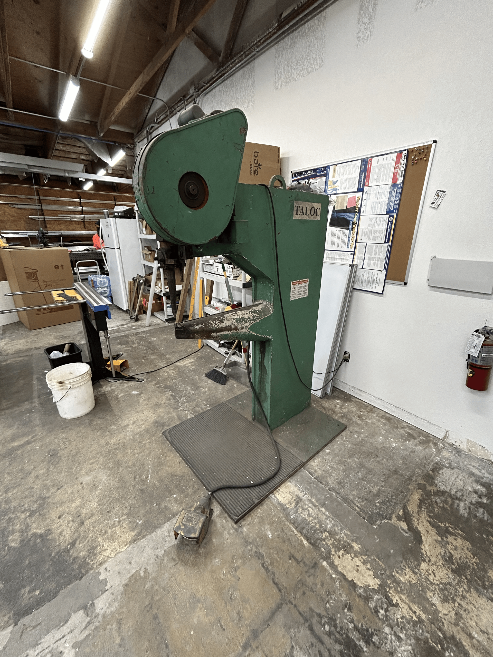 Green industrial press machine in a workshop with a foot pedal.