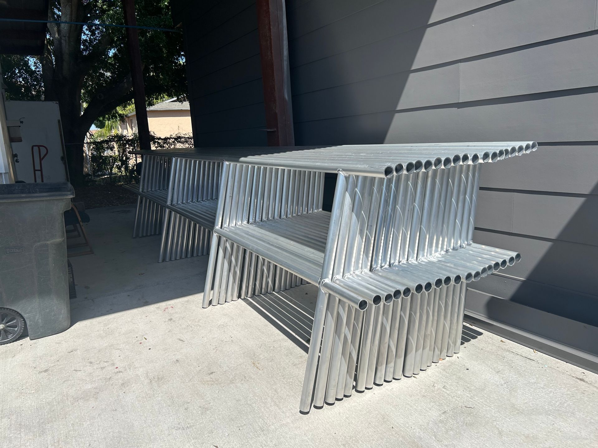 Stacked, silver metal tables outside a building on a concrete surface.