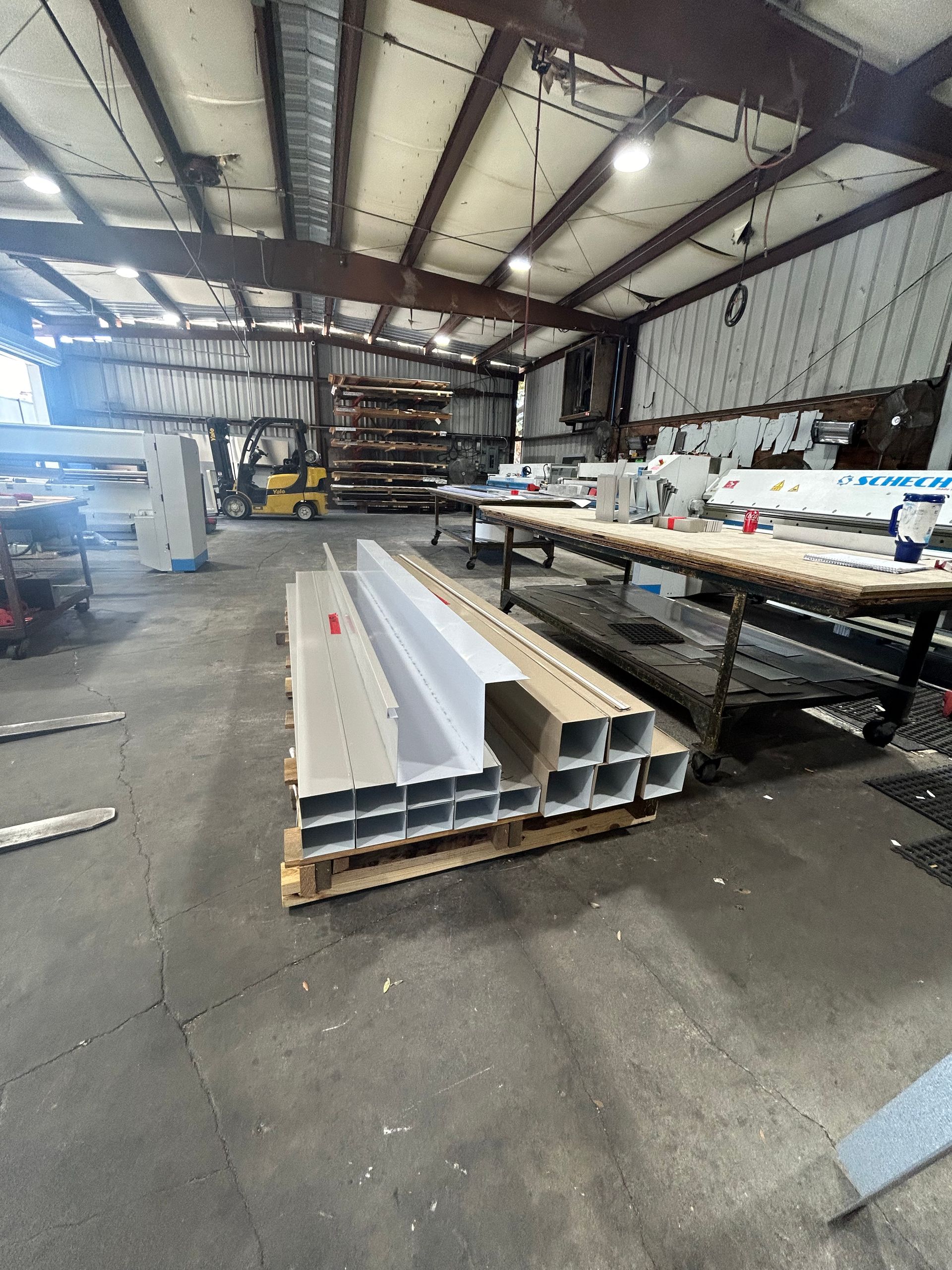 Warehouse interior with metal beams on a pallet. A forklift and machinery are visible.