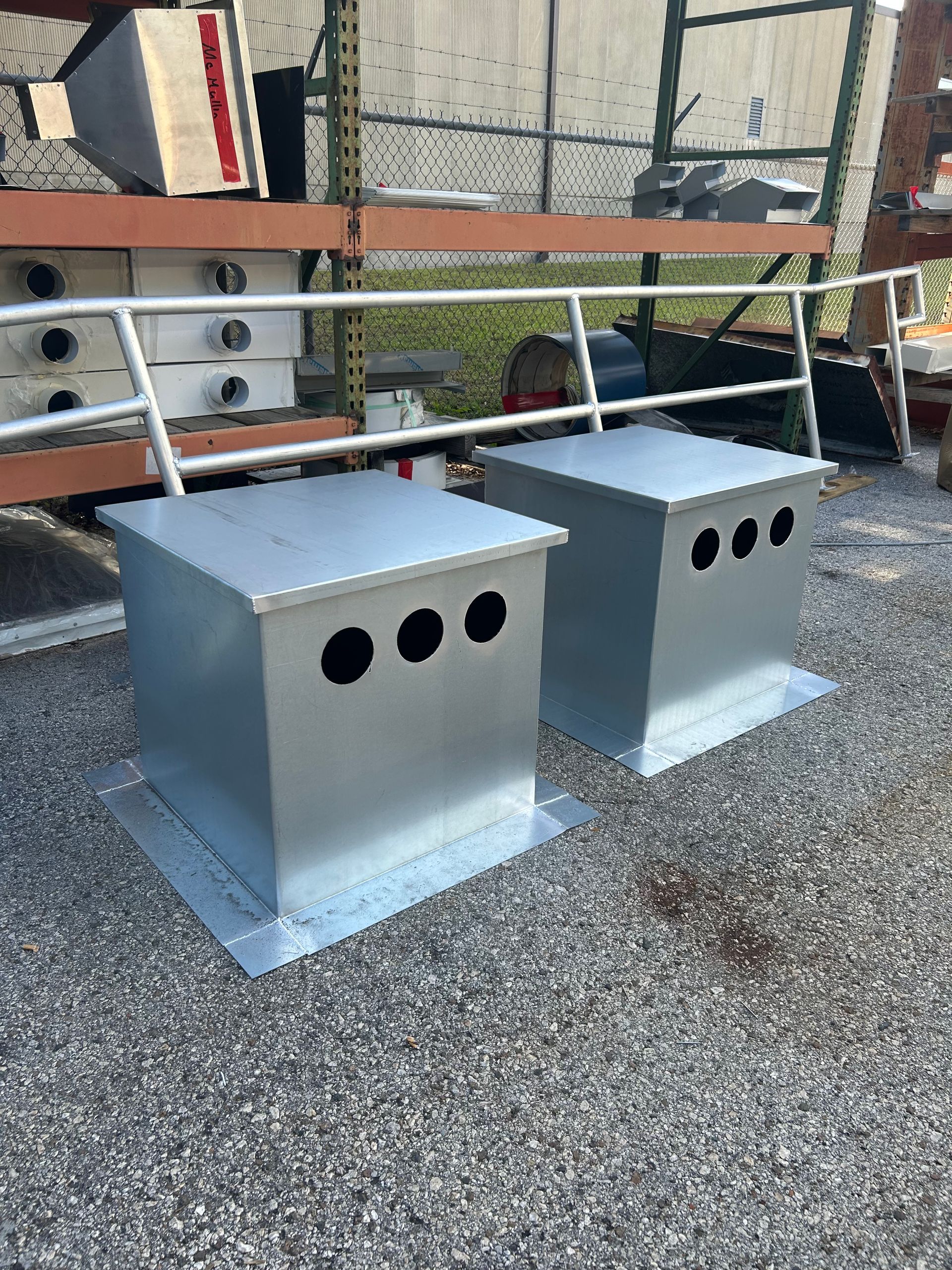 Two metallic gray square boxes with round holes sit on gravel.