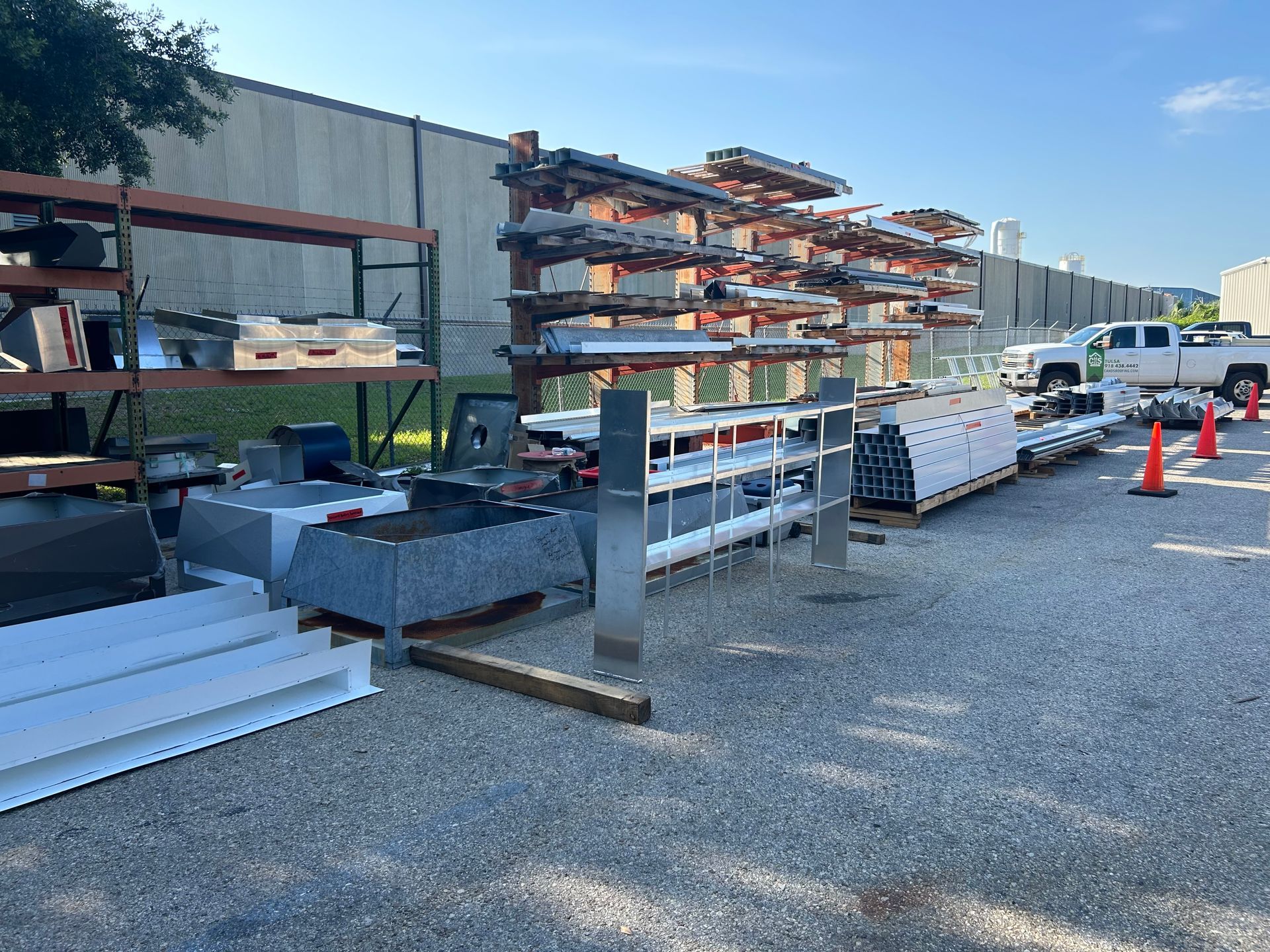 Outdoor storage of metal roofing materials on racks and pallets, with a white truck in the background.