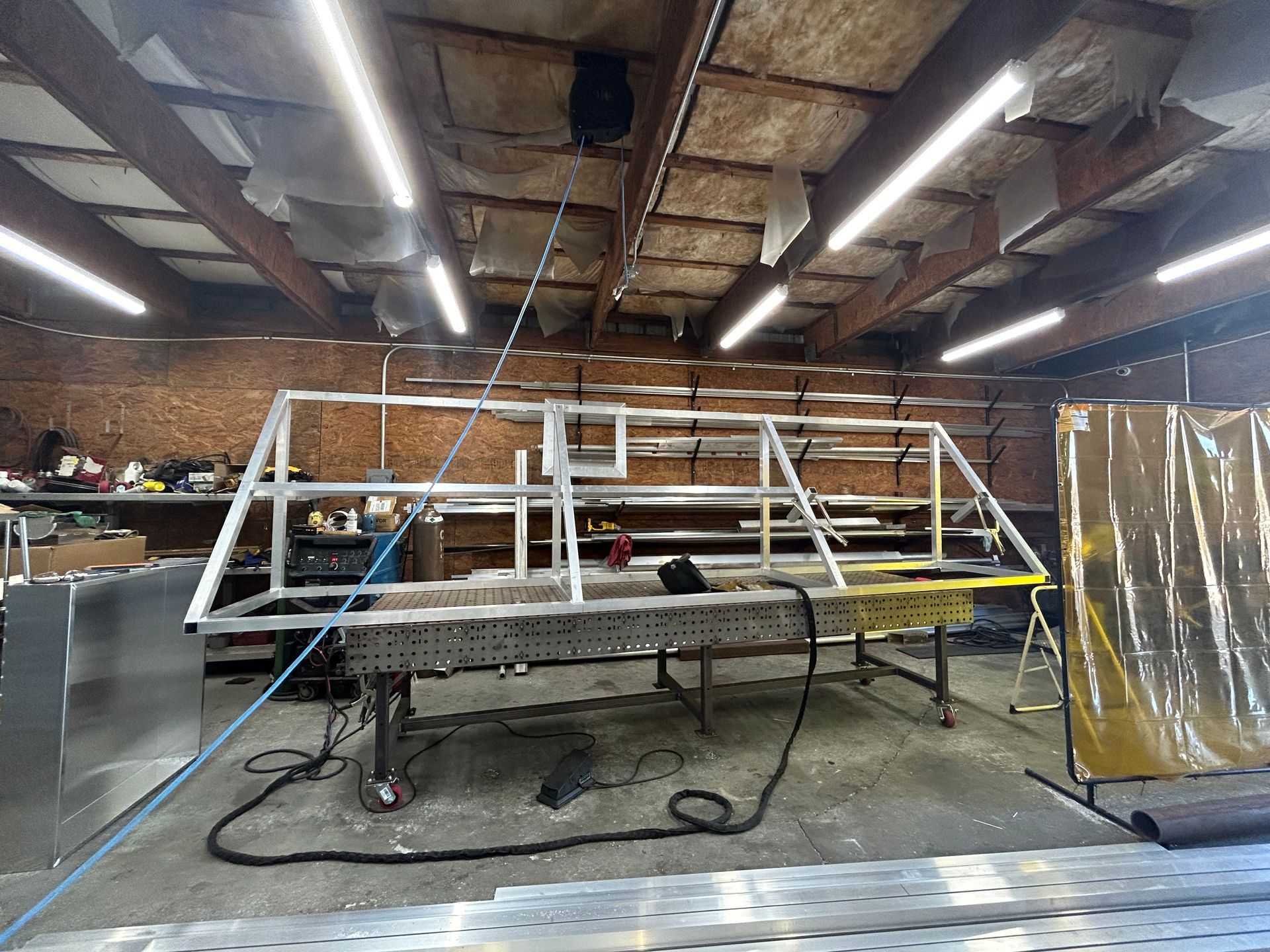 Metal frame being welded in a workshop, under fluorescent lights.