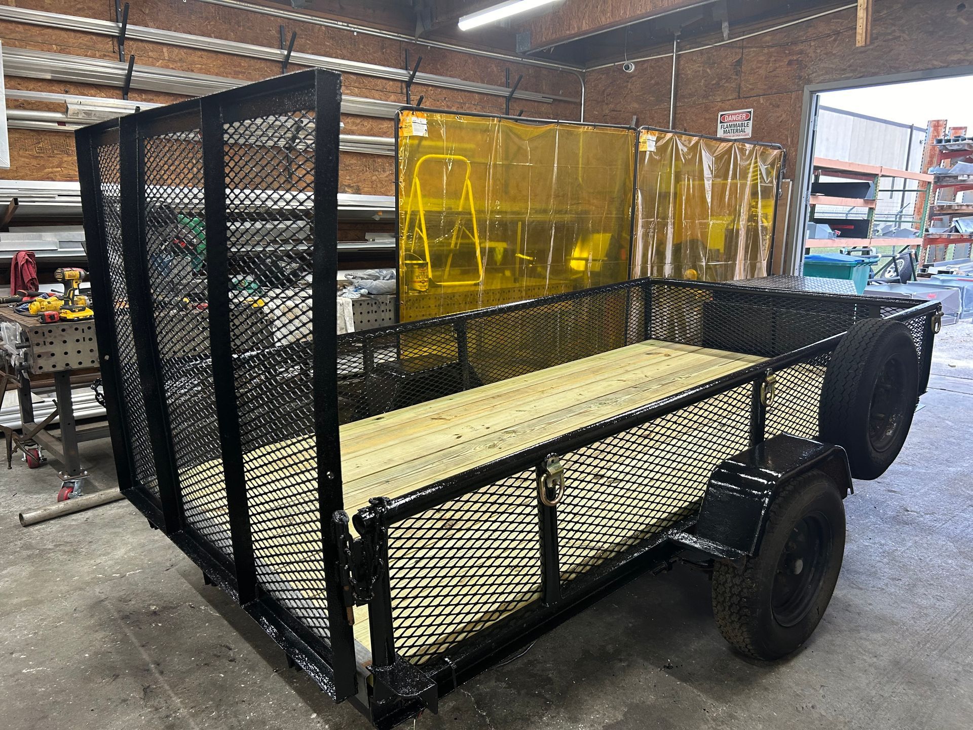Black utility trailer with mesh sides and wooden bed.