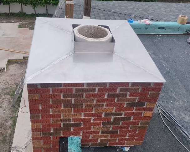 Brick chimney with a silver metal top and a concrete flue on a rooftop.