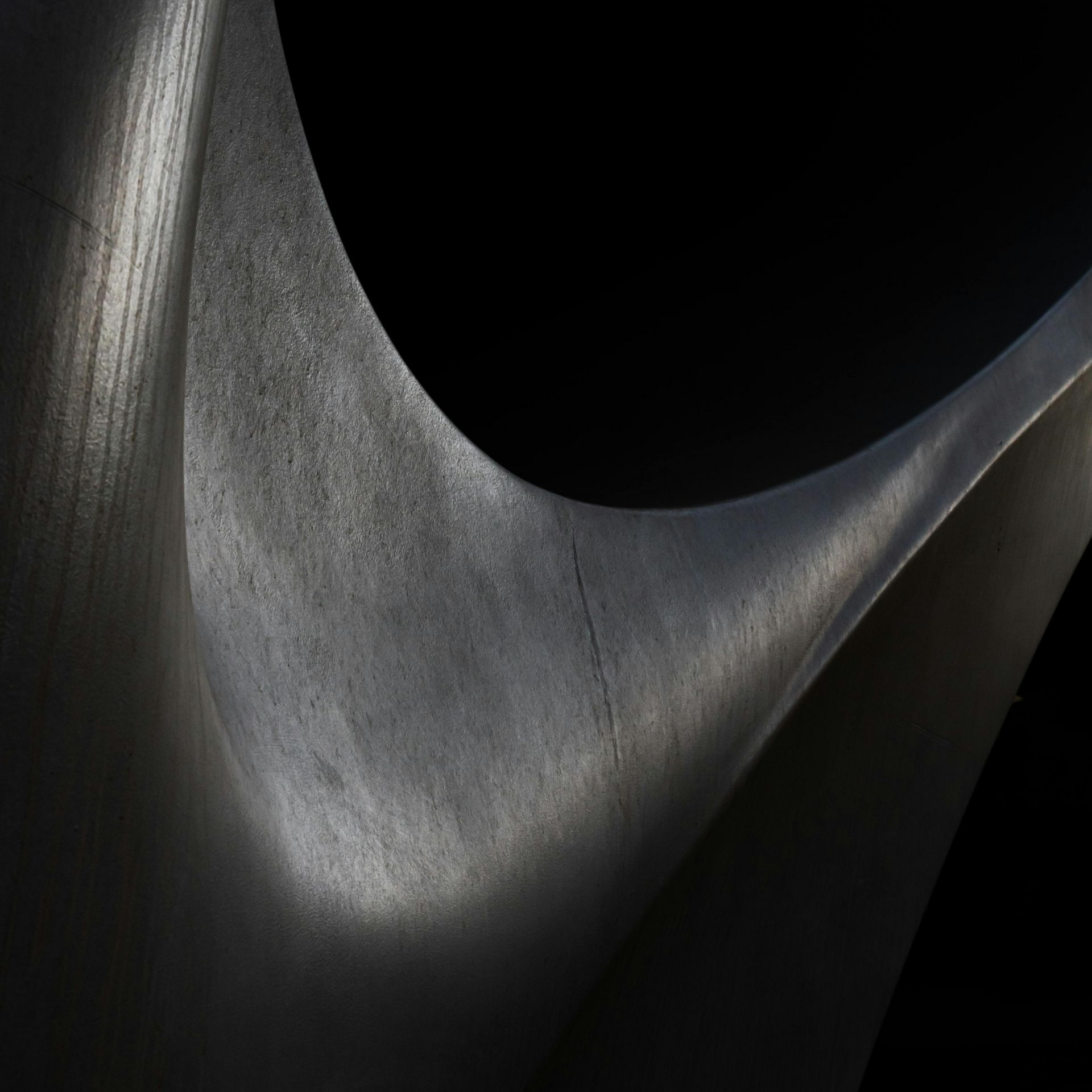 Abstract close-up of a textured, curved gray surface with highlights and shadows against a black background.