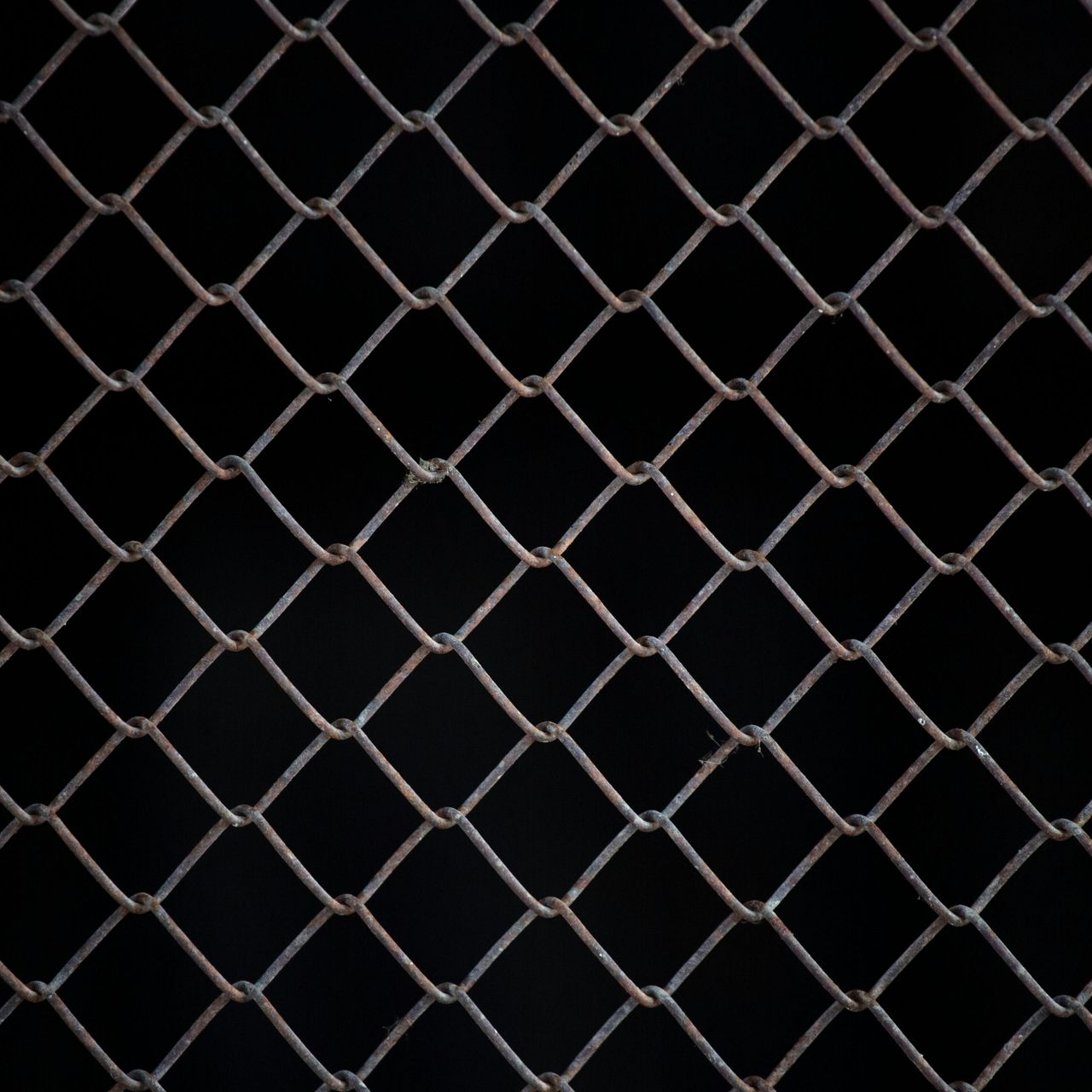 Rusty chain-link fence against a black background.