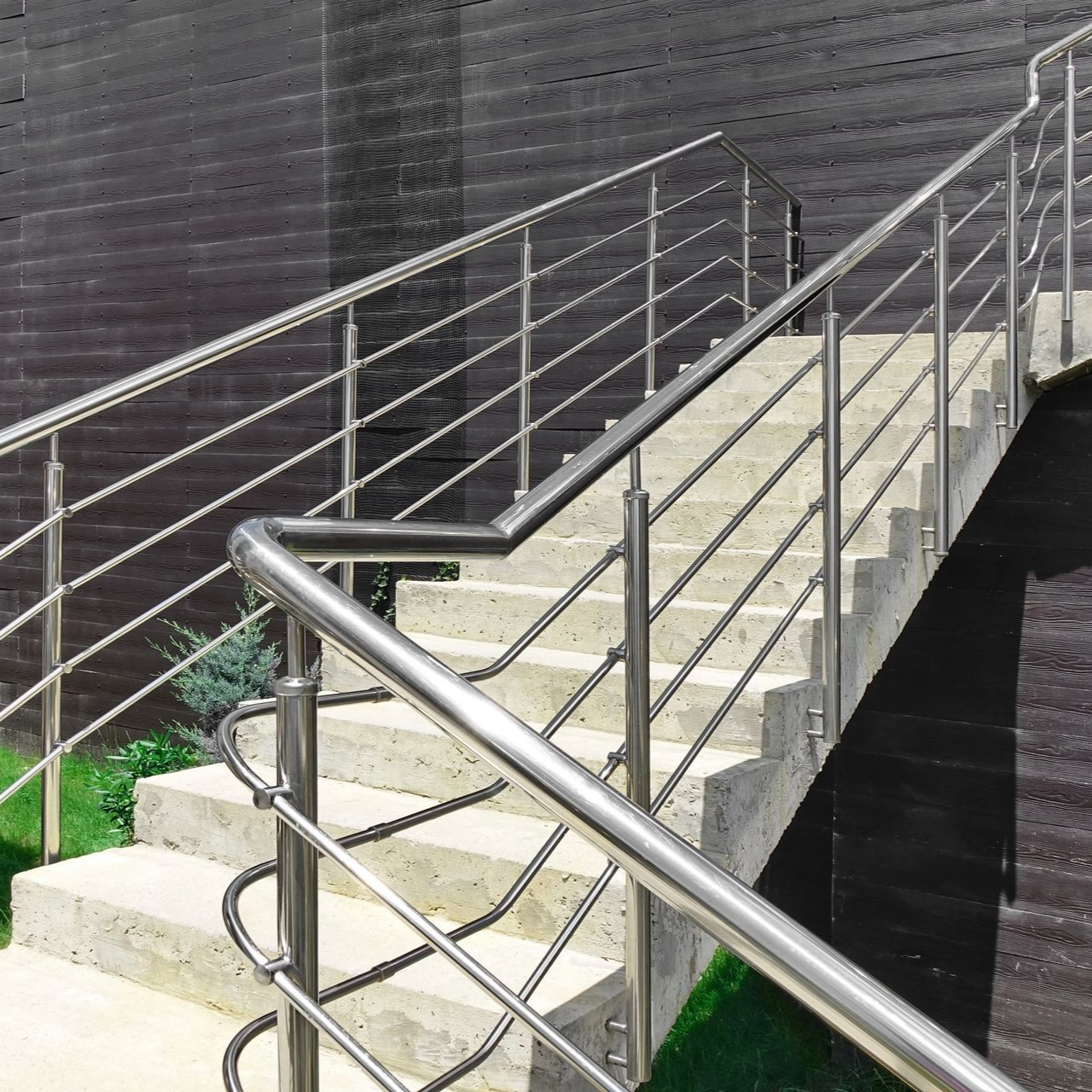 Concrete outdoor staircase with stainless steel railings against a dark wooden wall.