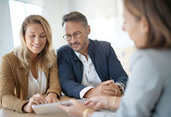 A man and a woman are sitting at a table looking at a tablet.