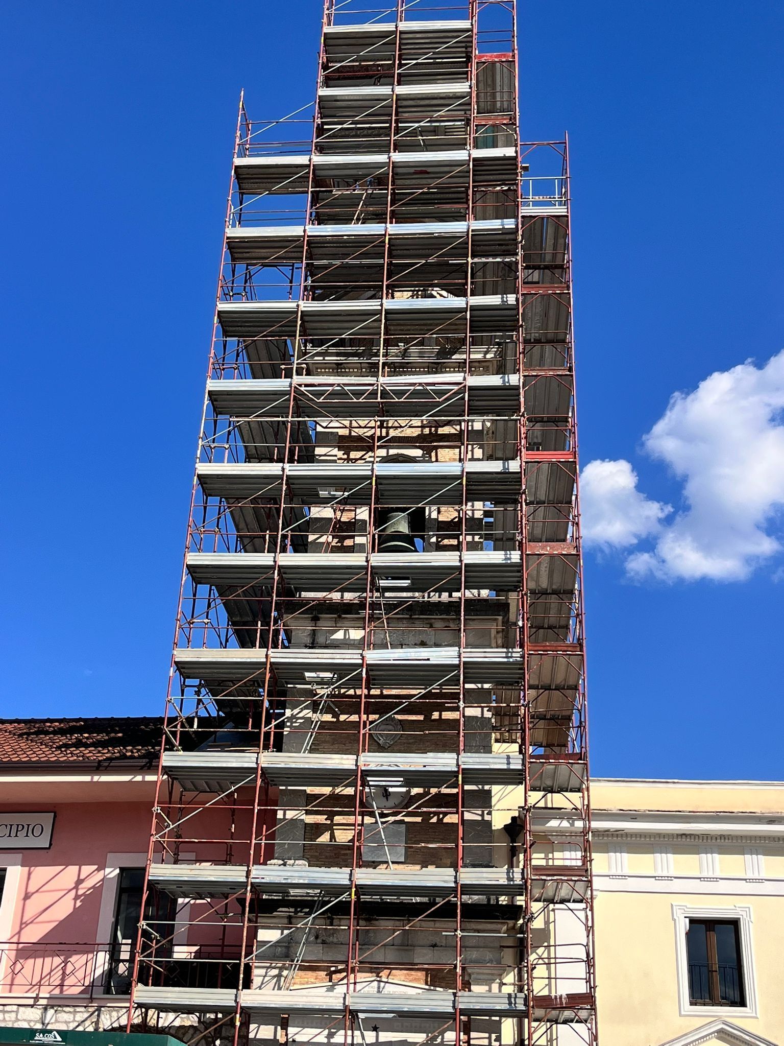 Un'impalcatura circonda un alto edificio contro un cielo azzurro, oscurandone parzialmente la facciata.
