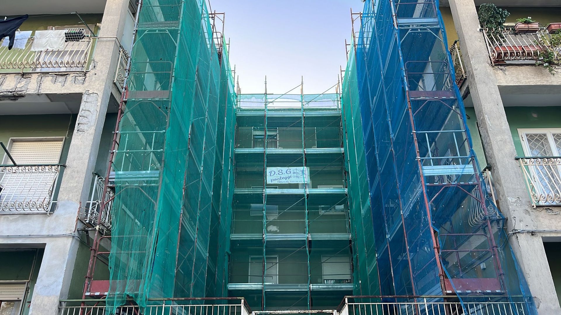 Impalcature ricoperte da reti verdi e blu sulla facciata esterna di un edificio in fase di ristrutturazione.