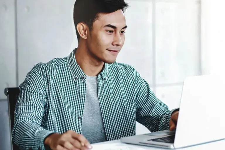 A woman wearing headphones is sitting at a desk using a laptop computer.