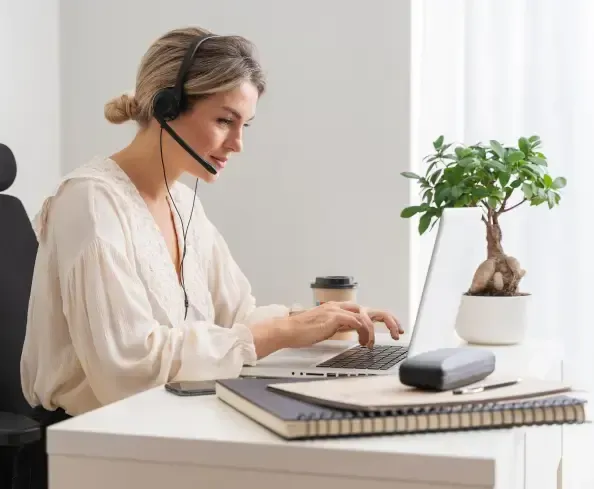 A woman wearing headphones is sitting at a desk using a laptop computer.