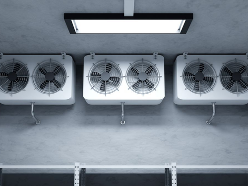 Three large white industrial cooling units mounted on a concrete wall beneath a fluorescent light.