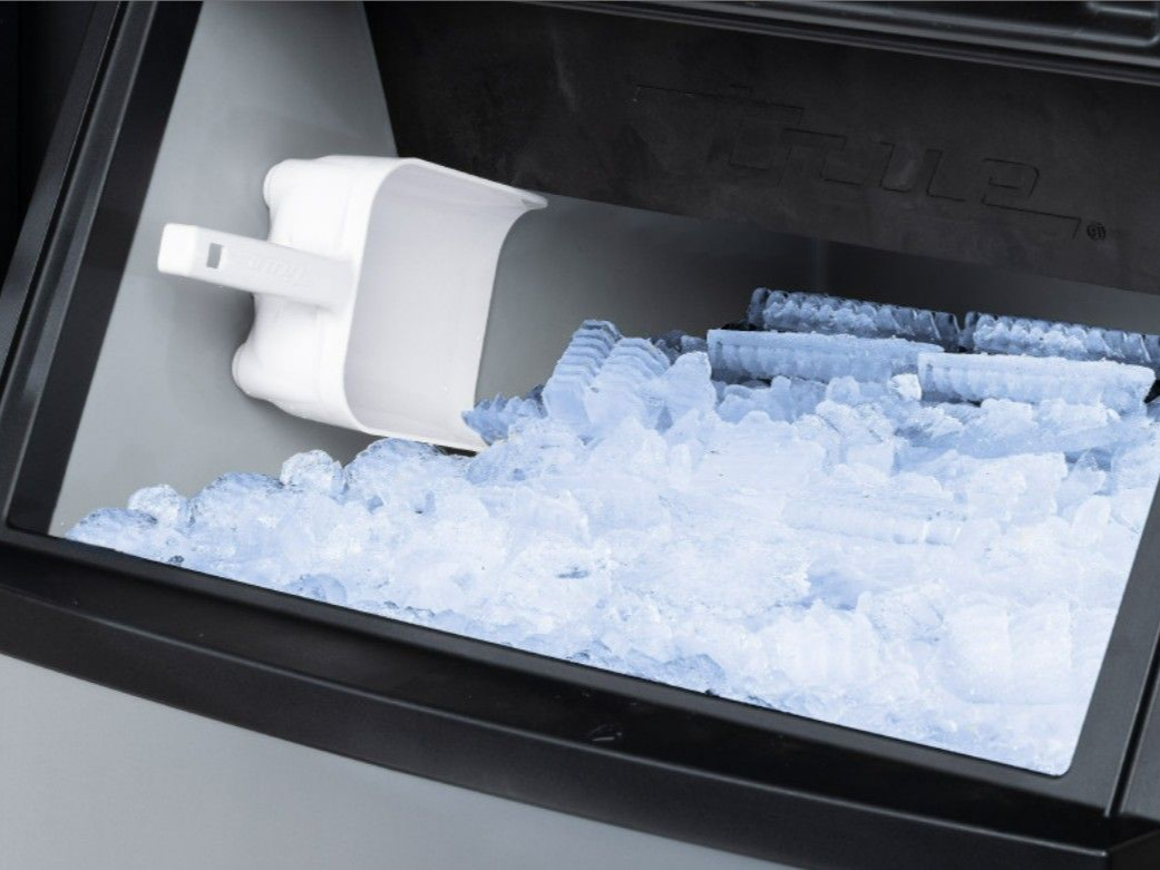 Ice maker drawer in a refrigerator filled with ice cubes and a scoop.