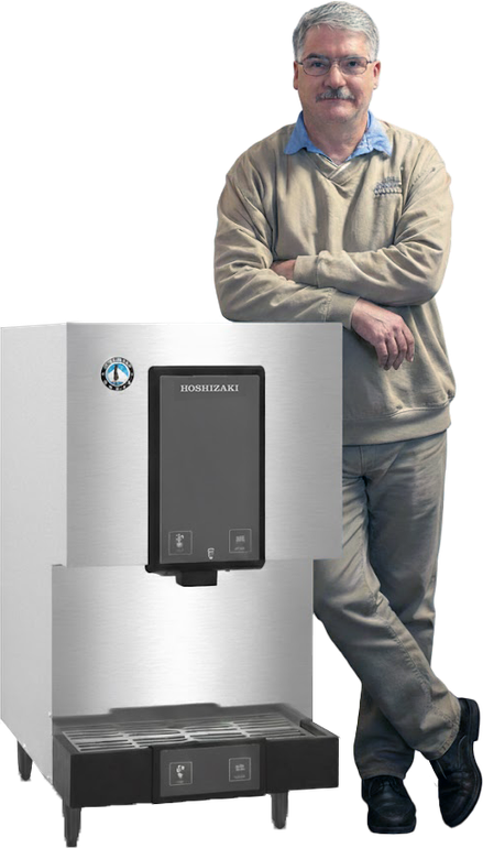 Man leans against an ice machine. He is wearing glasses, a sweater, and khaki pants. The machine is stainless steel.