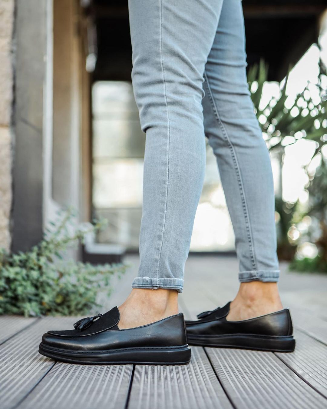 Una persona que viste un par de mocasines negros y jeans está parada en una terraza de madera.