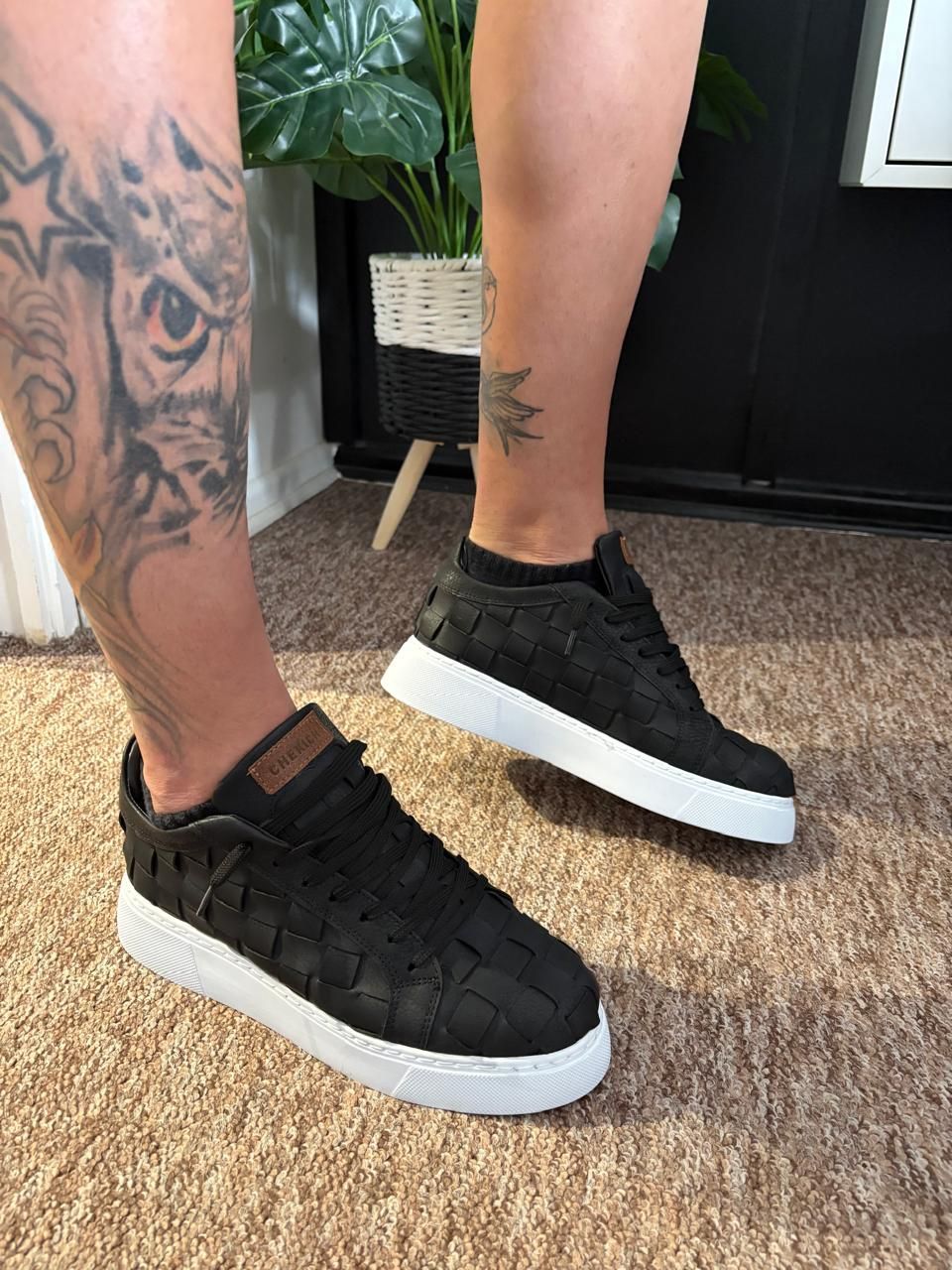 Una persona con un tatuaje en la pierna lleva un par de zapatillas negras.