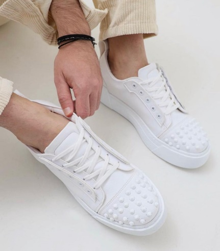 Una persona se ata sus zapatillas blancas con tachuelas en el lateral.