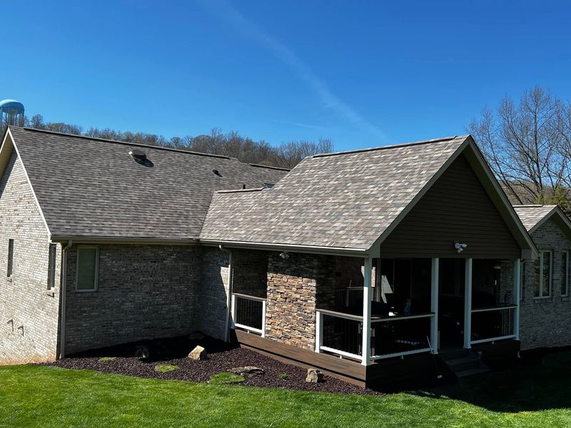 House with textured siding and roofing on a sunny day. Includes a porch and clear blue sky.