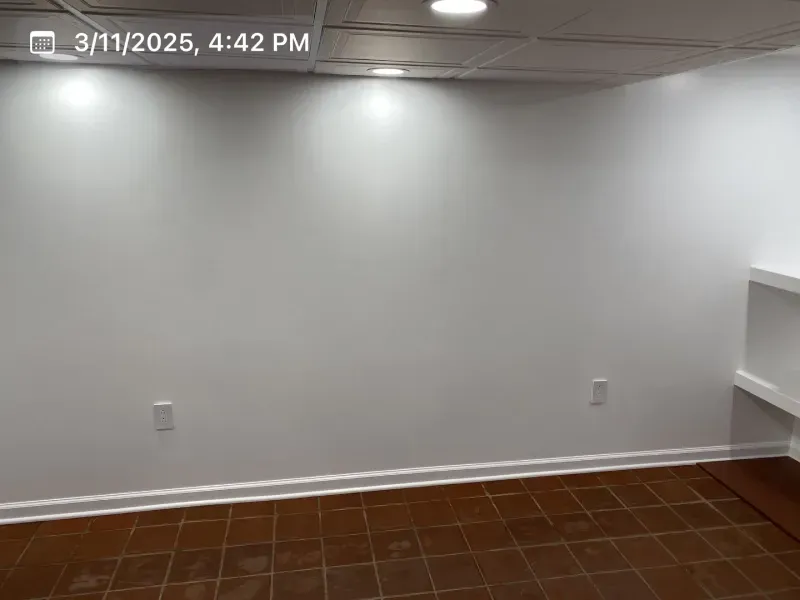 Empty white-walled room with brown tile floor; recessed lighting; built-in shelves on right wall.