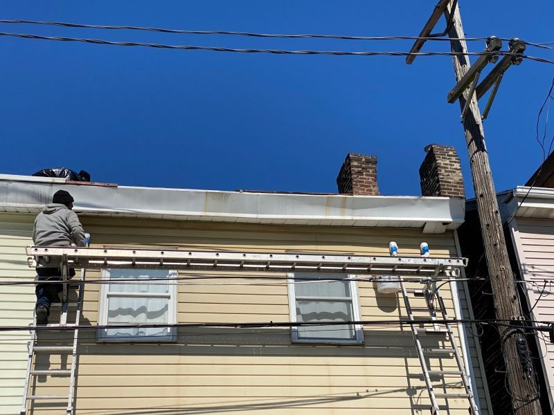 Person on ladder near two windows painting a building with a blue sky.