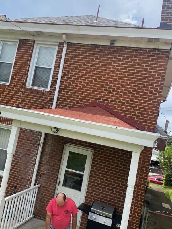 Brick building with white trim, red roof, and a man near a grill on a porch.
