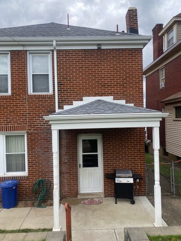 Red brick house exterior with white-framed door under a small canopy; a grill is to the right.