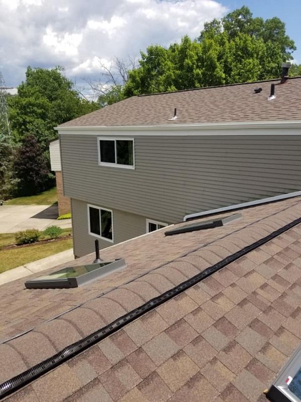 Brown shingled roof with a gray-sided house in the background and a blue sky.
