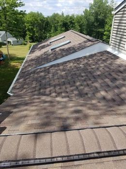 A brown shingled roof with three skylights, a white edge, and gutters.
