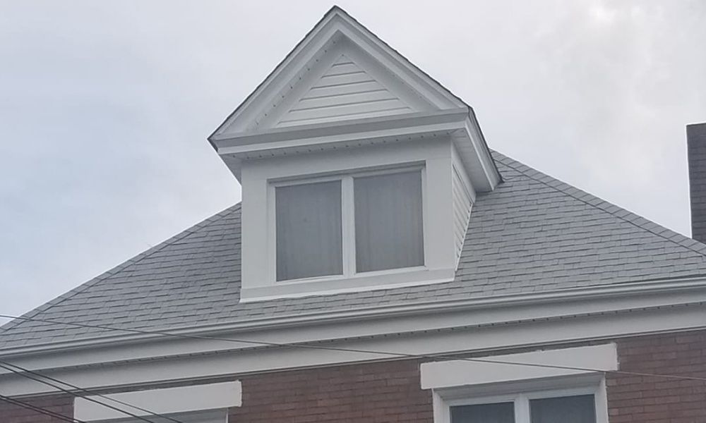 White dormer window on a gray shingled roof, against a cloudy sky.