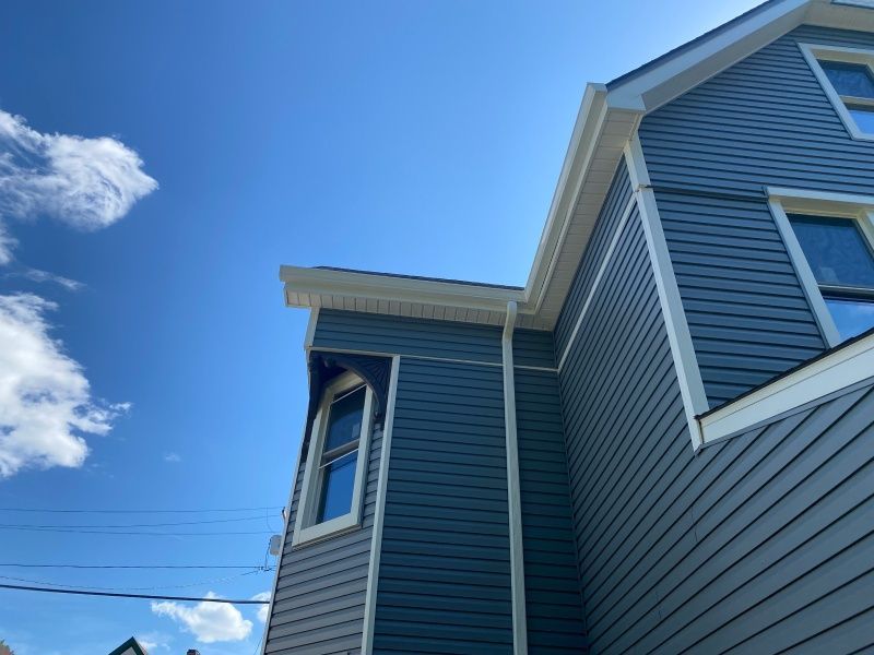 Blue house exterior with white trim against a blue sky, visible window and roof.