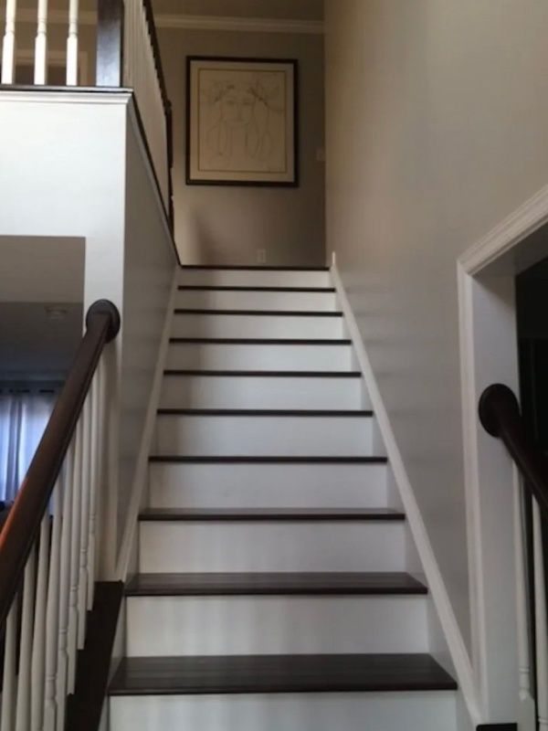 Staircase with white risers, dark treads, brown banister, and framed artwork on the wall.