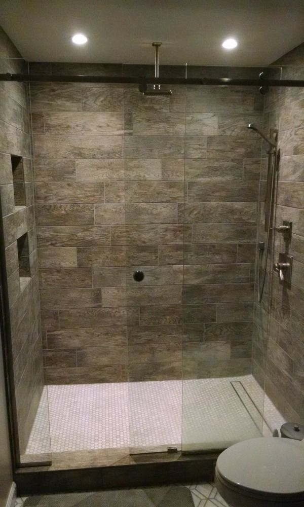 Walk-in shower with brown tile walls, glass door, and white tile floor. Recessed shelves and overhead lights.