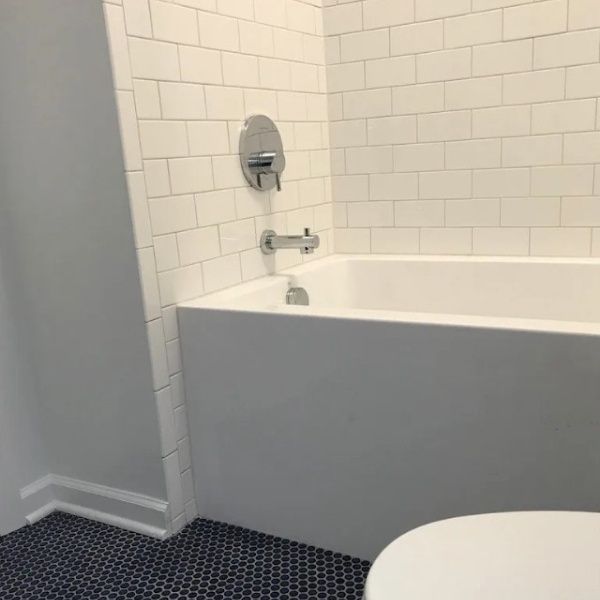 Bathroom with white tile walls, a white tub, and blue tiled floor.