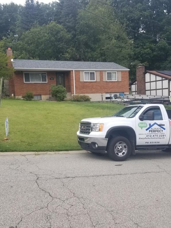 White truck parked in front of a brick house with a newly installed gray roof.